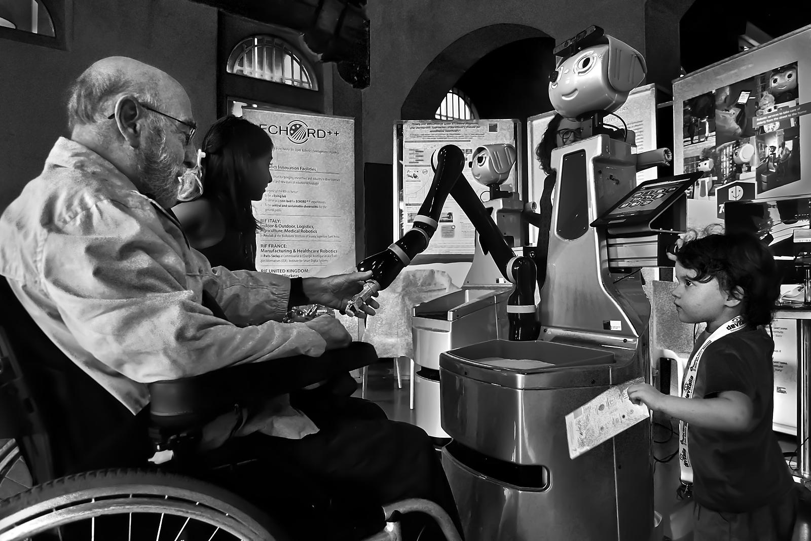 Un braccio robotico di servizio aiuta una persona anziana in carrozzina: robotica assistiva per l'autonomia quotidiana.